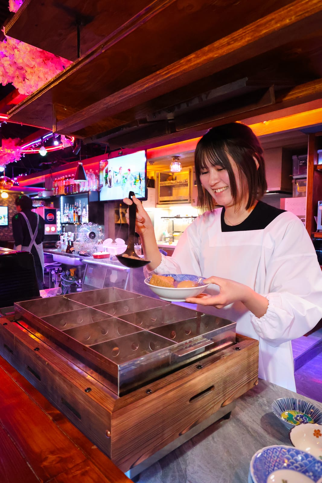 カウンターのおでん鍋からおでんをよそうスタッフ